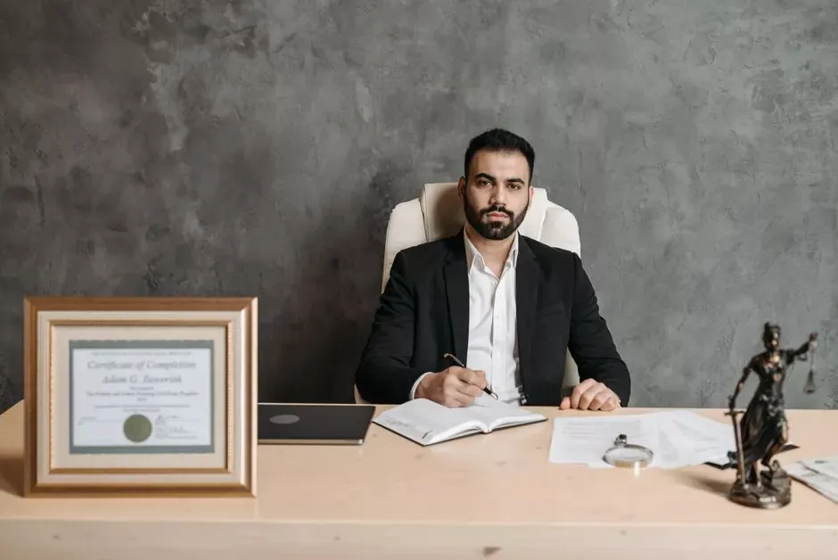 Confident man sitting at a desk surrounded by legal documents and a certificate.