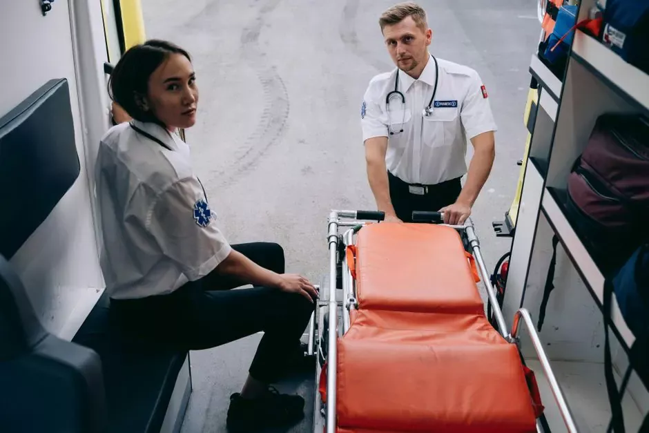 Two paramedics prepare a stretcher inside an ambulance, ready for an emergency response.